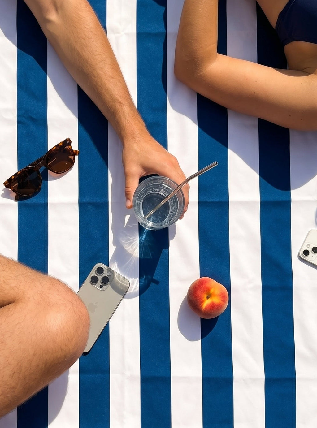 Friends relaxing on the Amalfi compact microfibre travel towel with blue and white stripes during a seaside picnic with fruit and drinks