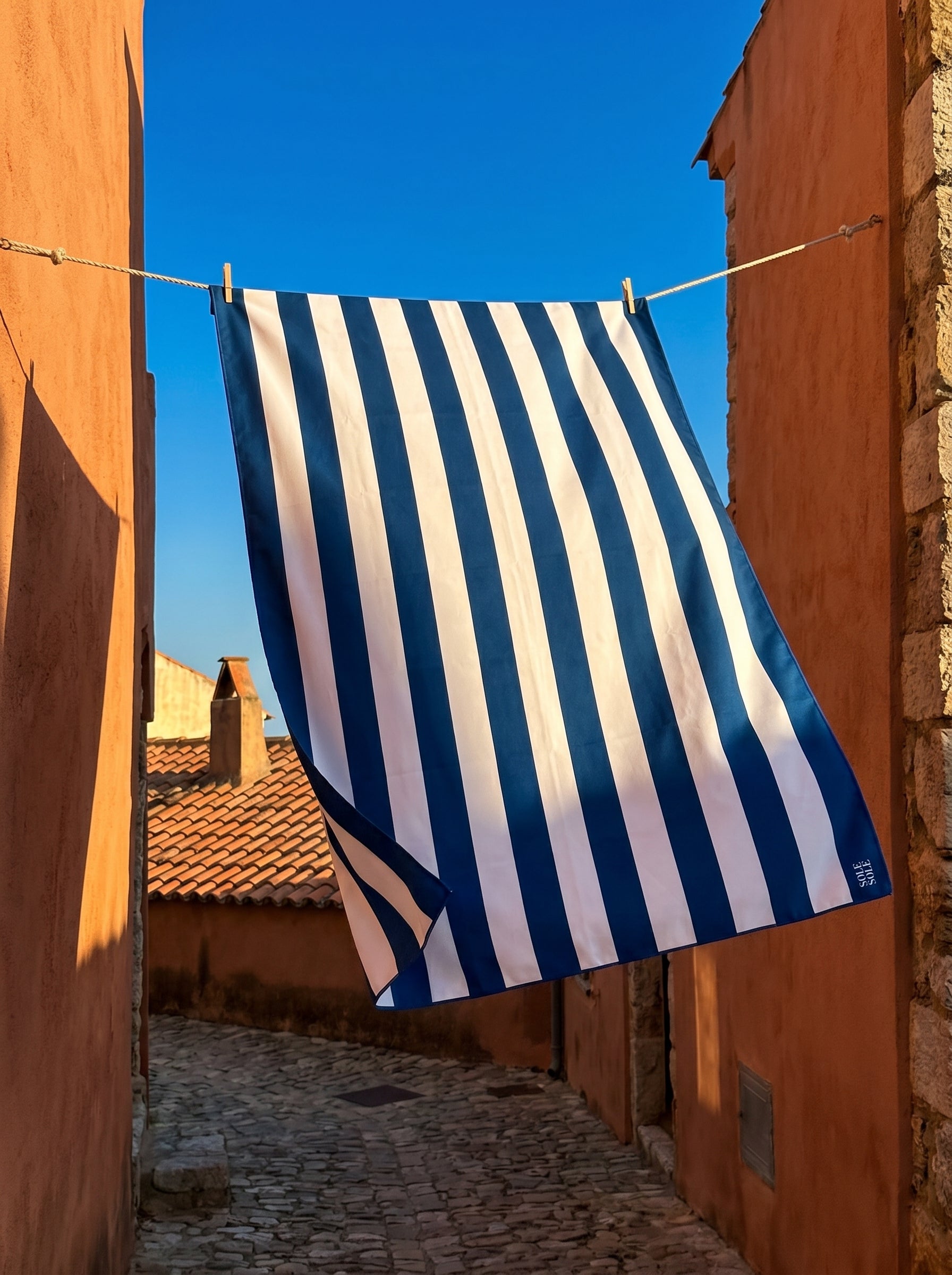 Amalfi quick-dry microfibre travel towel with blue and white stripes hanging on a clothesline during golden hour