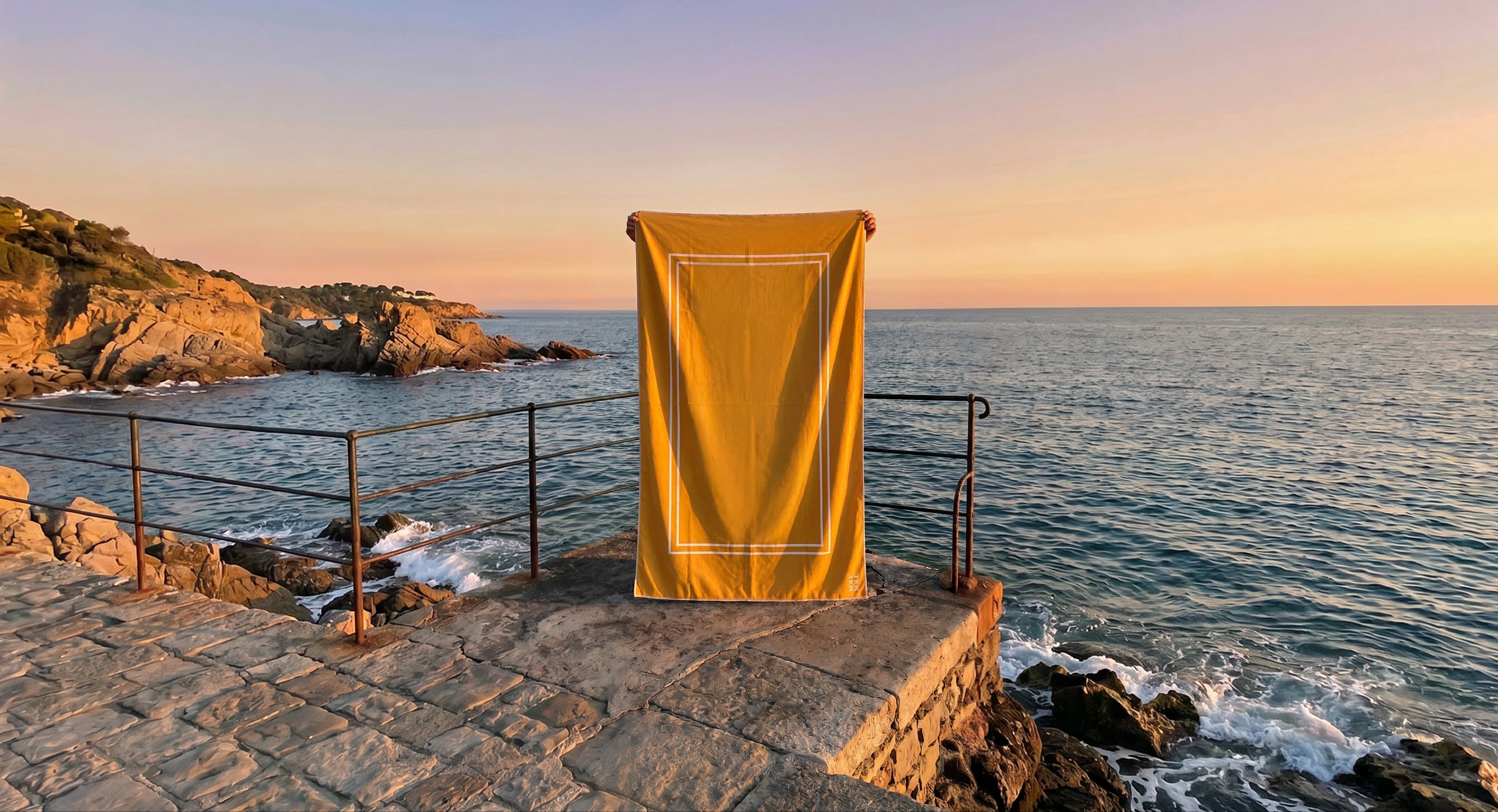 Capri yellow microfibre travel towel held up against coastal backdrop, lightweight and quick-dry beach towel