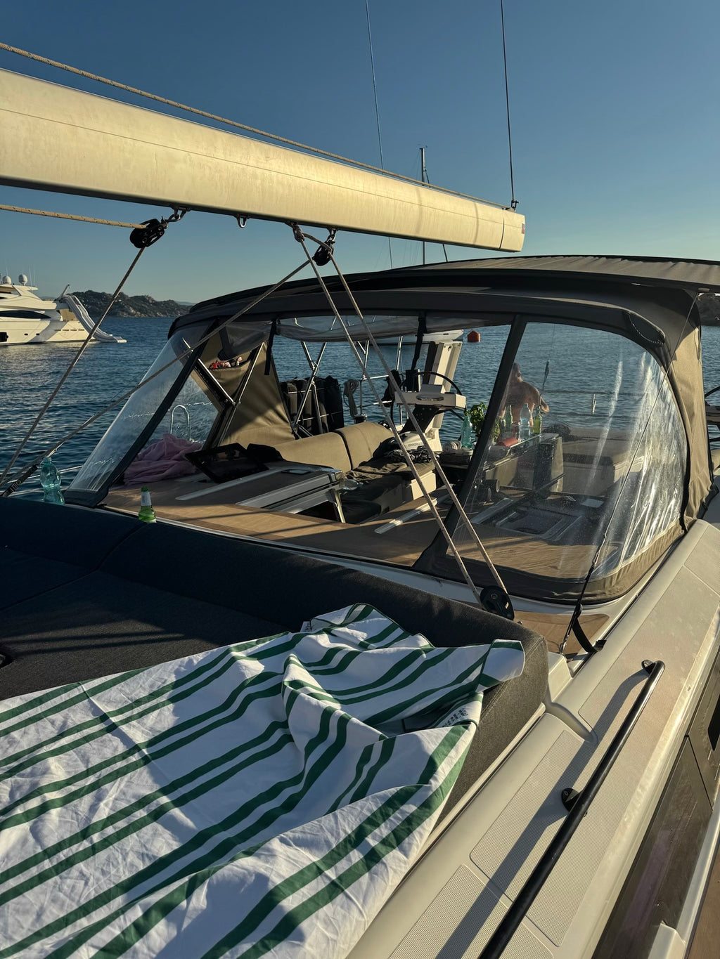Positano quick-dry and compact microfibre travel towel with white and dark green stripes displayed on a sailing boat daybed at golden hour